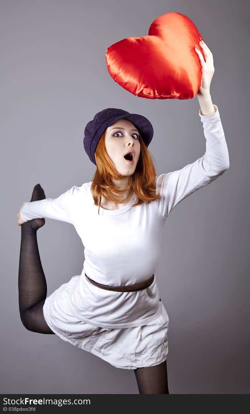 Beautiful red-haired girl in cap with toy heart. Studio shot.