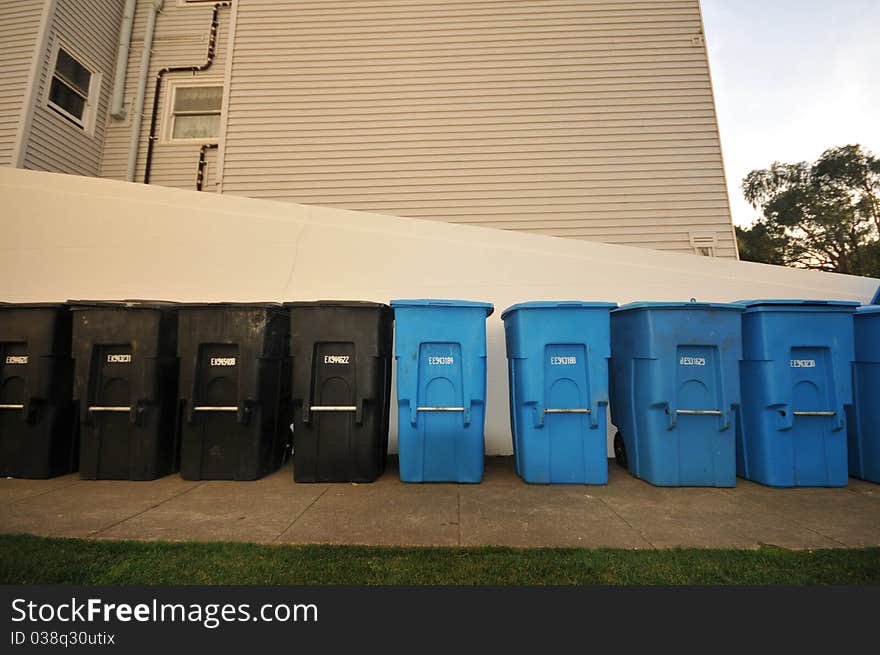 A row of recycling and garbage cans next to a wall. A row of recycling and garbage cans next to a wall