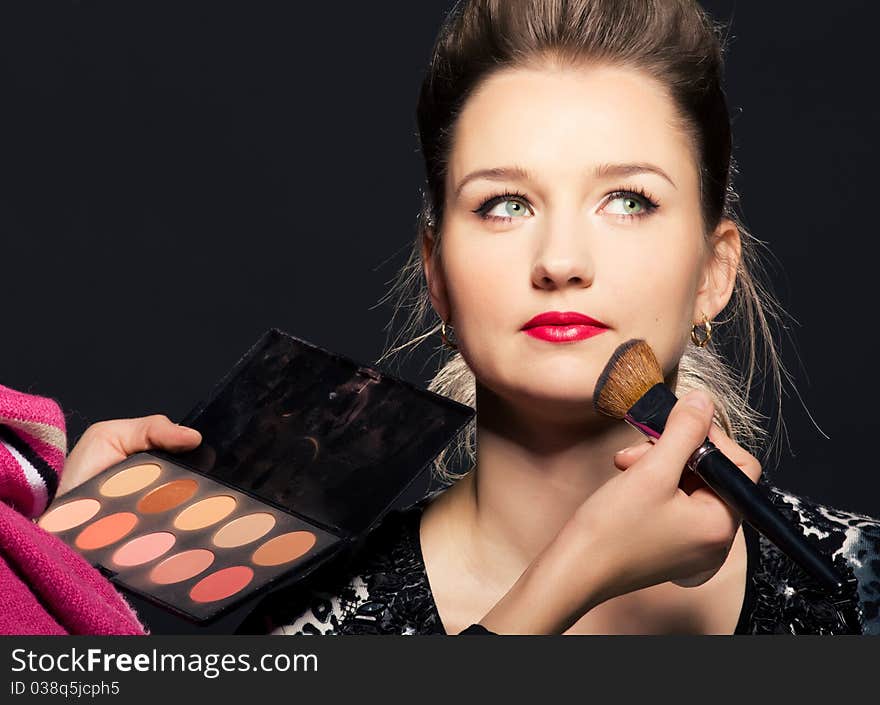 Charming young woman applying blusher eyelid. Close-up view.