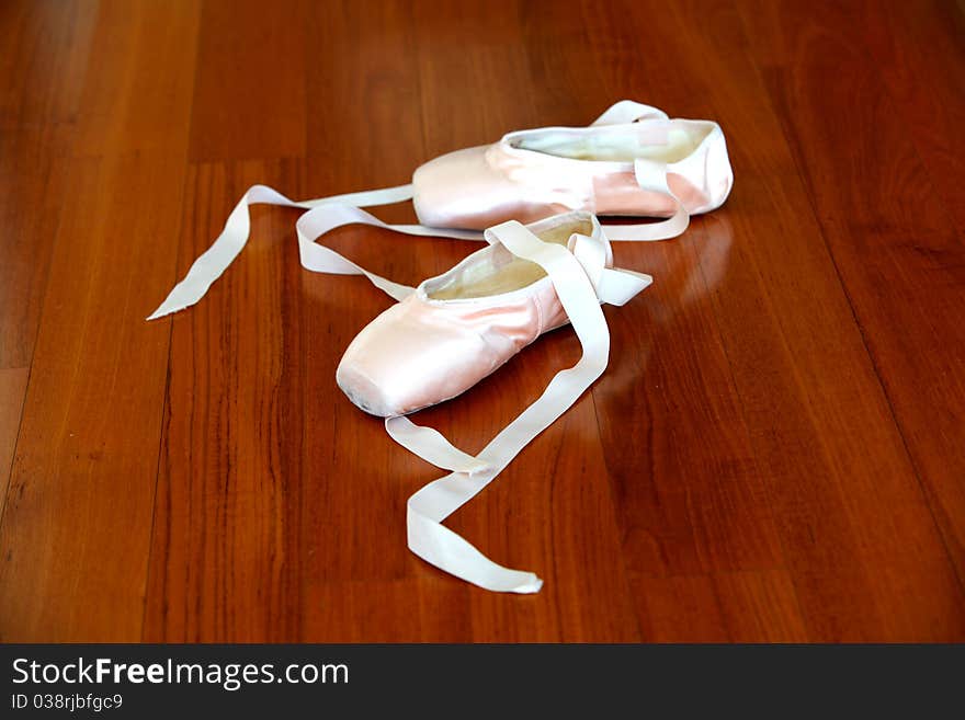 Ballet pointe shoes of pink satin on the wooden studio floor.