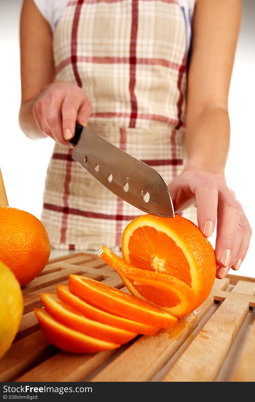 Girl cutting orange with the knife, on a wooden plate