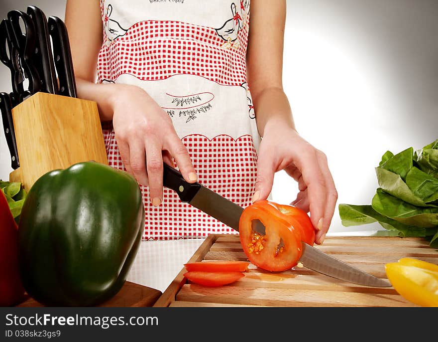 Girl cutting tomato with the knife, on a wooden plate. Girl cutting tomato with the knife, on a wooden plate