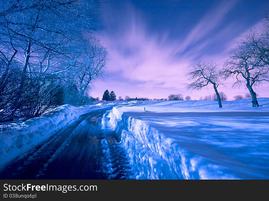 A beautiful blue and lavender nighttime scene along a snow covered road. A beautiful blue and lavender nighttime scene along a snow covered road