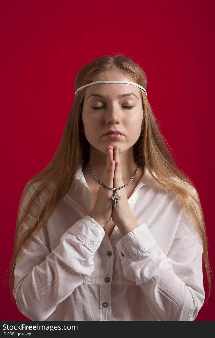 Young woman in a white shirt with a cross on a silver chain  praying. On red background. Young woman in a white shirt with a cross on a silver chain  praying. On red background.