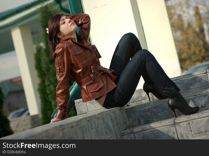 A sitting beautiful young girl is in a brown jacket. A sitting beautiful young girl is in a brown jacket