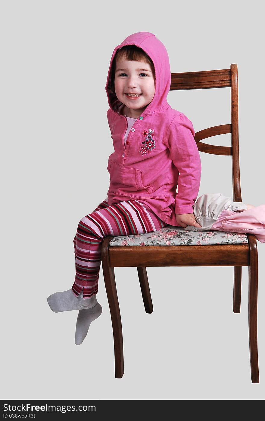 A nice little girl in a coat sitting on a chair and smiling into the camera, on whit background. A nice little girl in a coat sitting on a chair and smiling into the camera, on whit background.