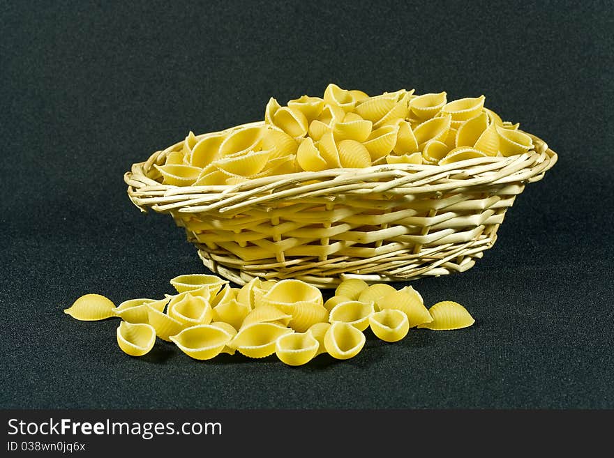 A closeup of a wicker basket containing uncooked shell pasta on a black background. A closeup of a wicker basket containing uncooked shell pasta on a black background