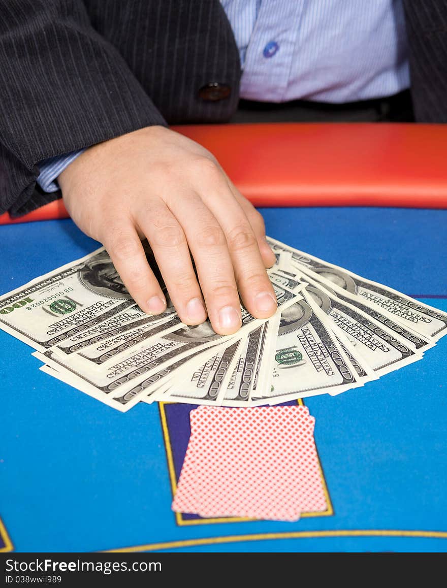 Close up of men's hand with cards and one hundred dollars banknotes on poker table. Close up of men's hand with cards and one hundred dollars banknotes on poker table