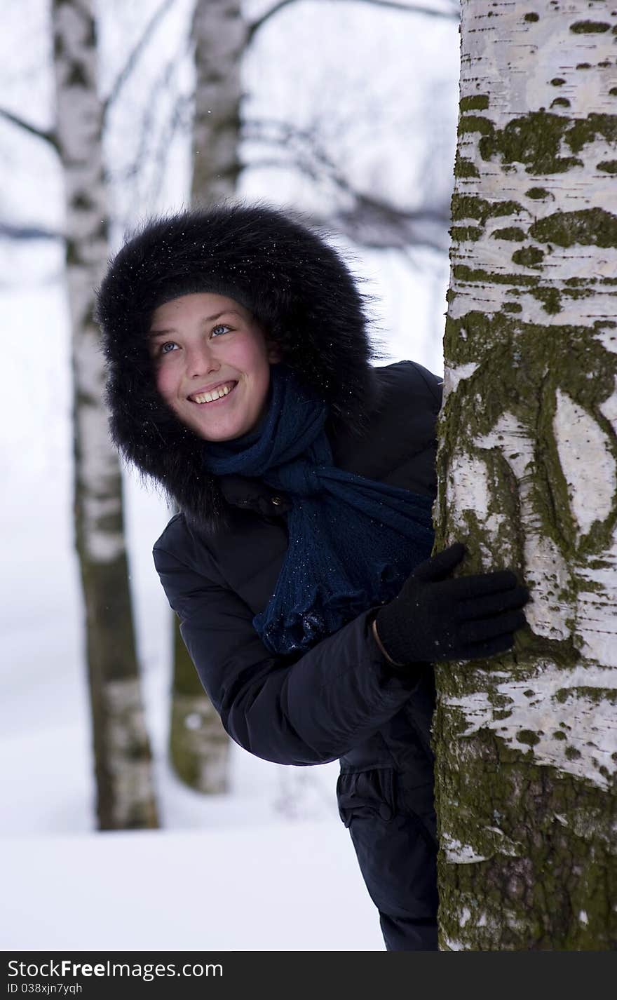 Young girl in the hood looks out from the tree. Young girl in the hood looks out from the tree