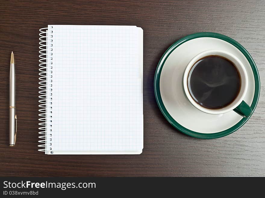 Notebook, silver pen and coffee in green cup on desk. Notebook, silver pen and coffee in green cup on desk