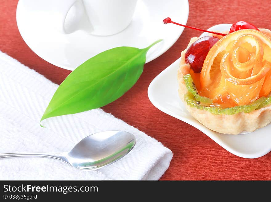 Closeup of cupcake with jelly and fruits on a white plate and a cup of coffee on a brown background. Closeup of cupcake with jelly and fruits on a white plate and a cup of coffee on a brown background