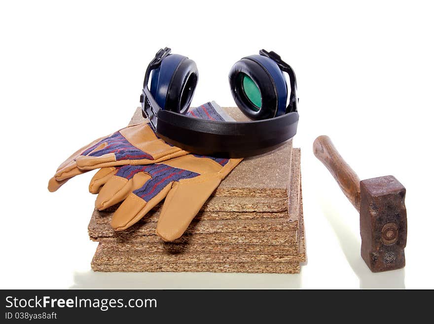 A hammer and working gloves and ear protection on top of a stack of wooden planks isolated over white