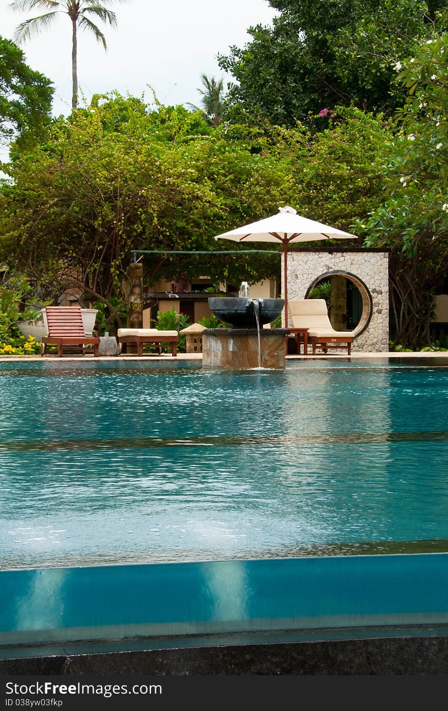 A tropical infinity pool with water bubble, water fountain and pool side bed on a tropical greenery background. Picture taken in a resort along Kuta beach in Bali, Indonesia.