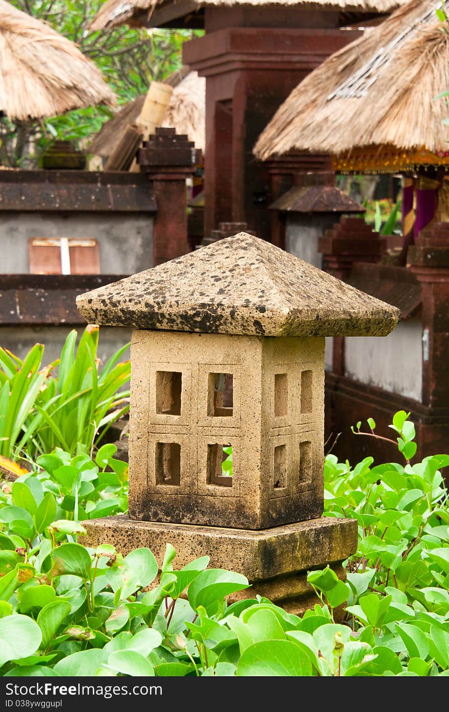 A garden decorative stone granite lamp in a middle of a dense vegetation. A garden decorative stone granite lamp in a middle of a dense vegetation