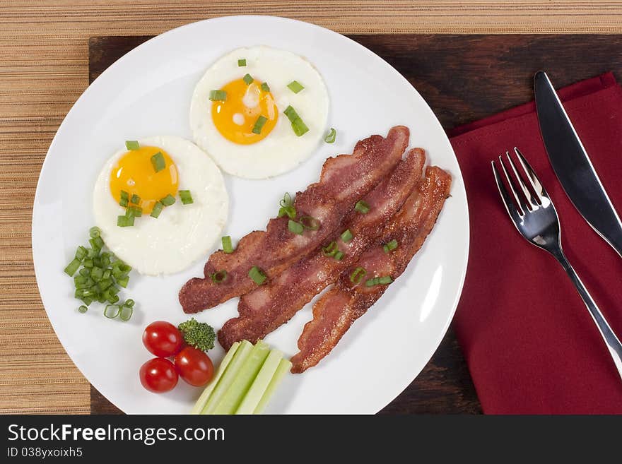 Fried eggs with fried bacon and vegetables.