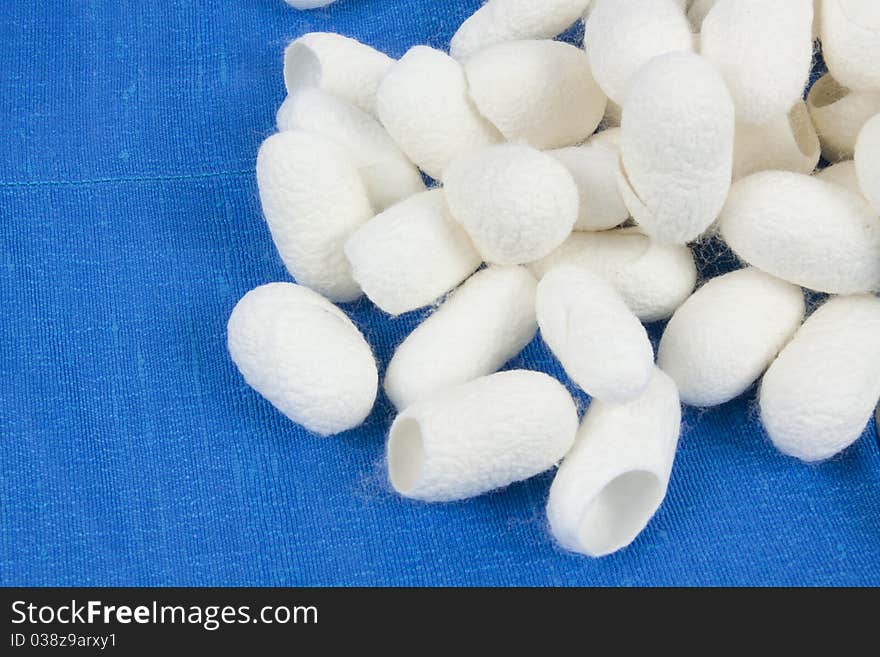 A pile of silkworm cocoons on the blue silk fabric.