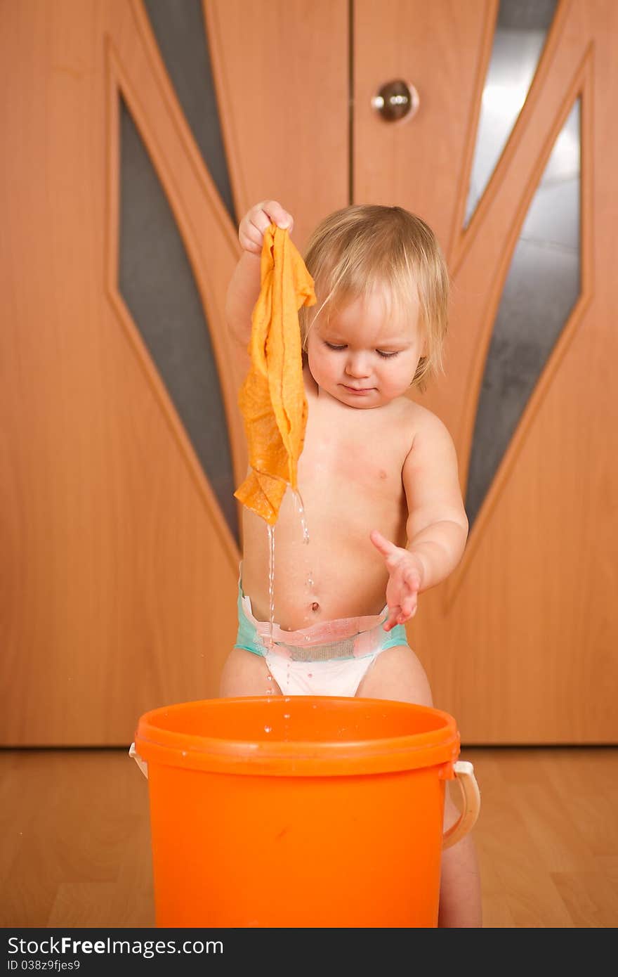 Adorable baby holding wet rug after washing it in orange pail