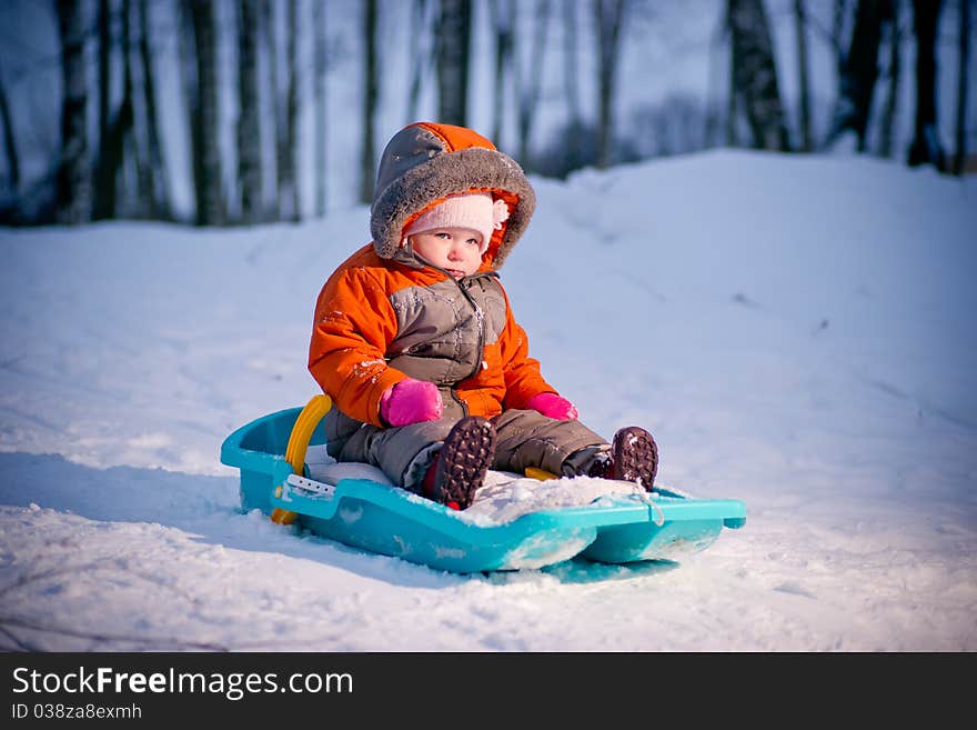 Serious baby sliding on sleigh from hill