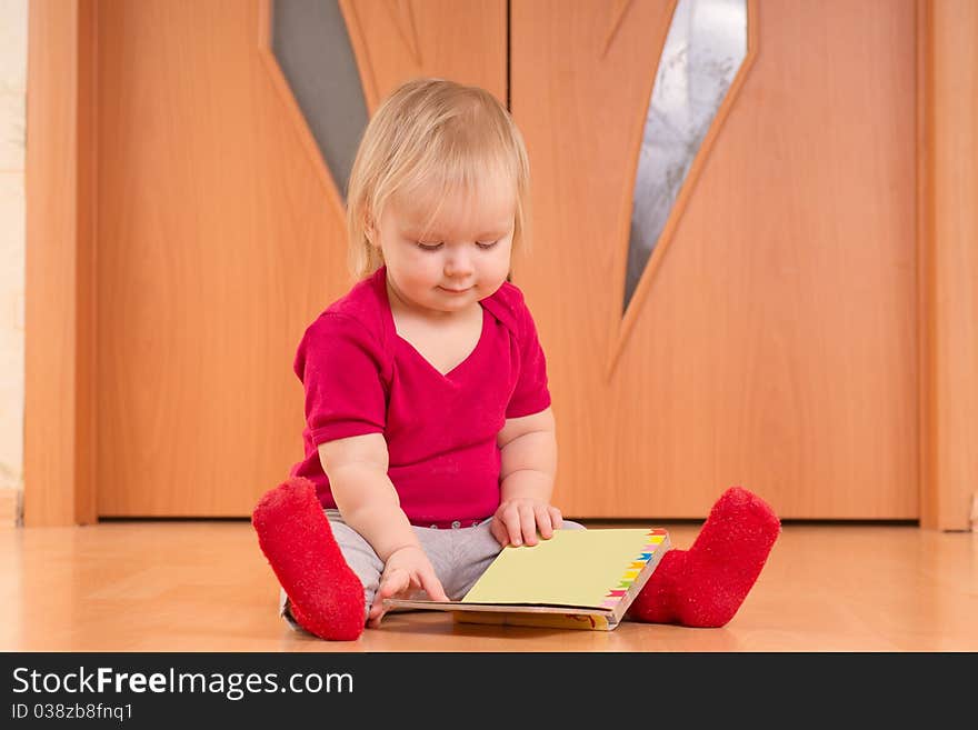 Adorable baby sit on floor and read small baby book. Adorable baby sit on floor and read small baby book