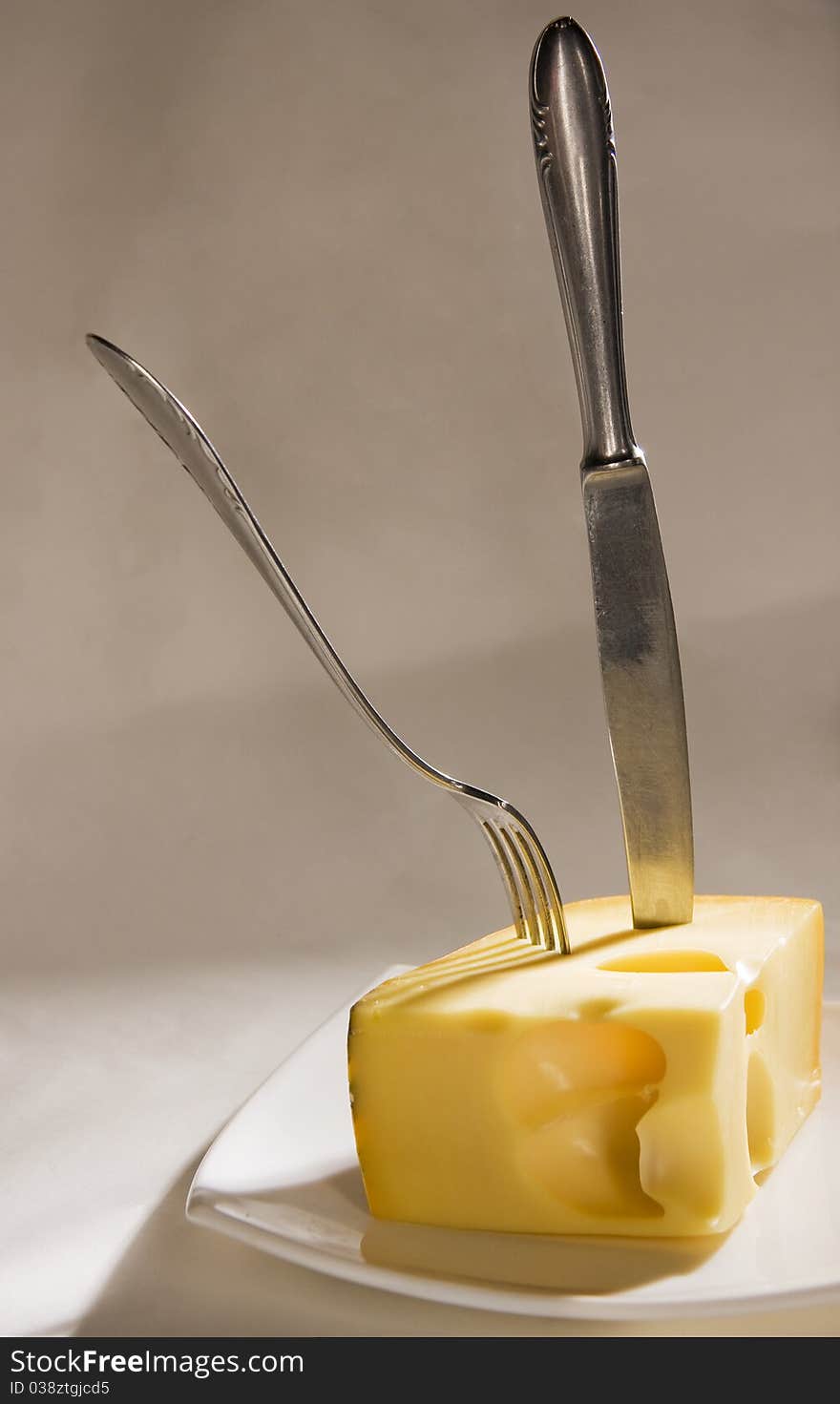 Knife and fork stick in cheese on grey background. Knife and fork stick in cheese on grey background