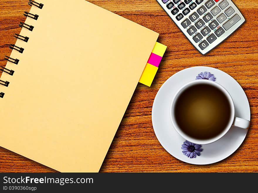 White cup of coffee and calculator on notebook on wood table background. White cup of coffee and calculator on notebook on wood table background