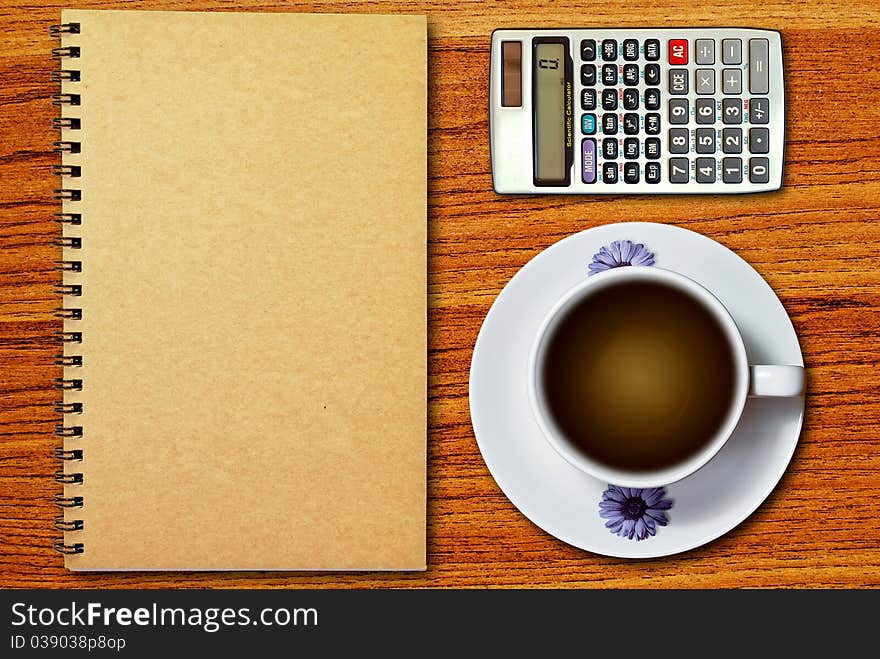 White cup of coffee and calculator on notebook on wood table background. White cup of coffee and calculator on notebook on wood table background