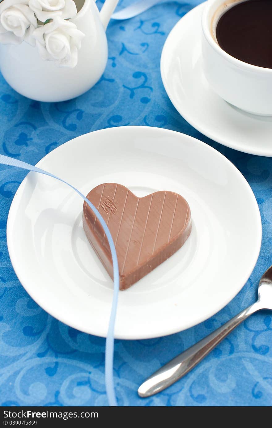 Chocolate heart, cup of coffee and white roses on a blue background. Chocolate heart, cup of coffee and white roses on a blue background