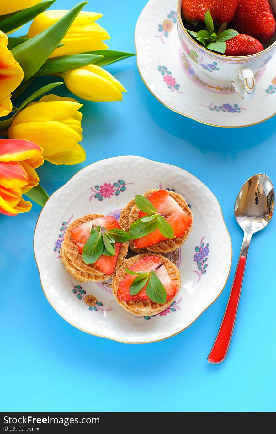 Cakes with fresh strawberry and mint and yellow tulips on blue background