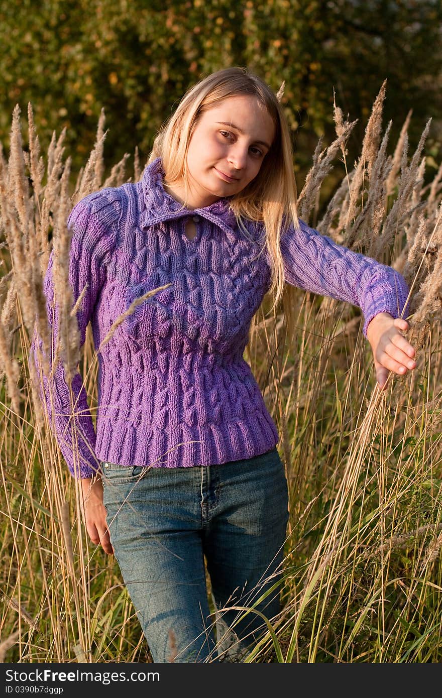 A girl in a lilac pullover and jeans in grass. A girl in a lilac pullover and jeans in grass