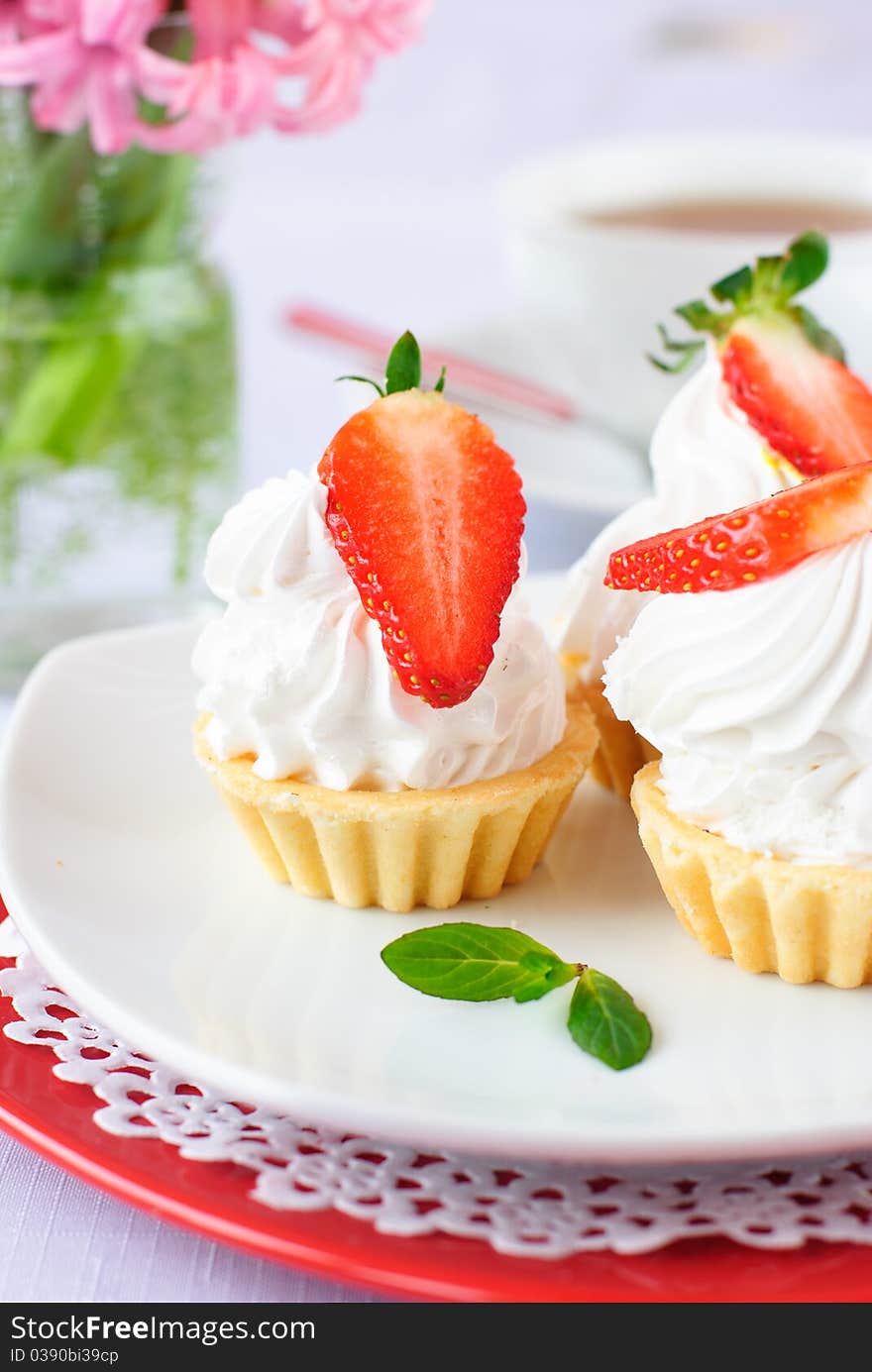 Cake with white protein cream and strawberry on white plate and soft background filled with white cup of tea and hyacinth flowers