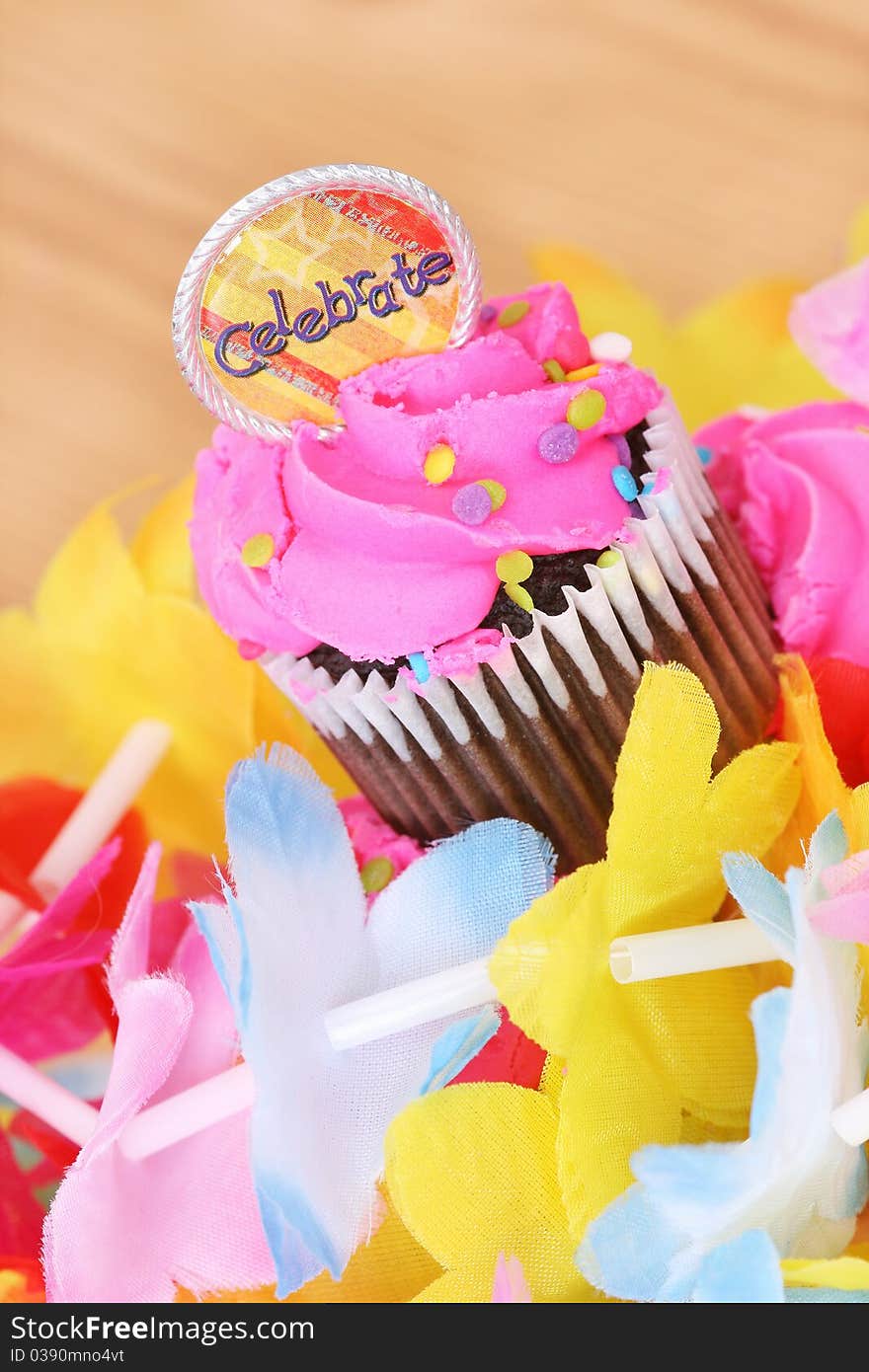 Cupcake with pink icing and celebrate medallion surrounded by a colorful lei. Cupcake with pink icing and celebrate medallion surrounded by a colorful lei