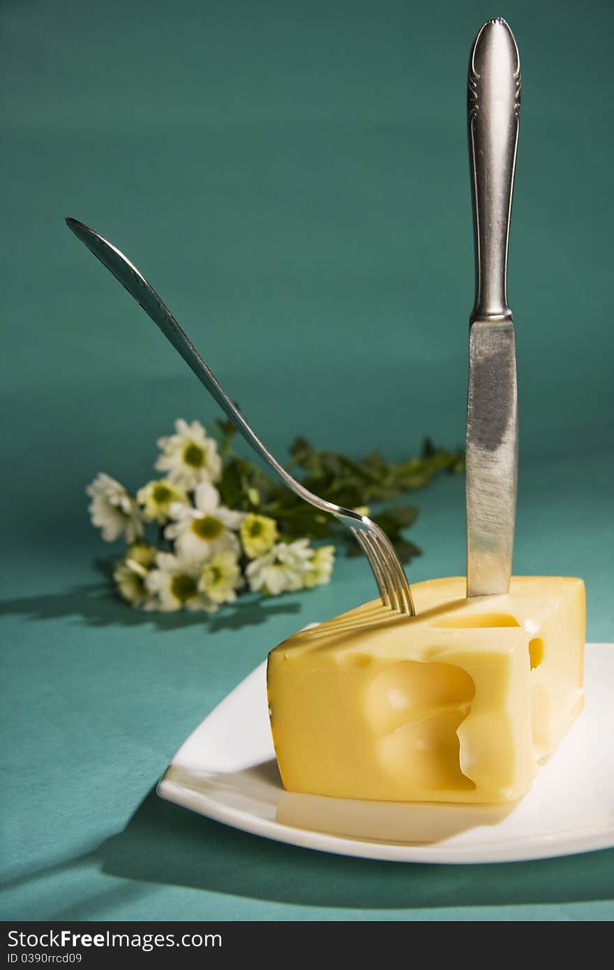 Knife and fork stick in cheese on cyan background. Knife and fork stick in cheese on cyan background