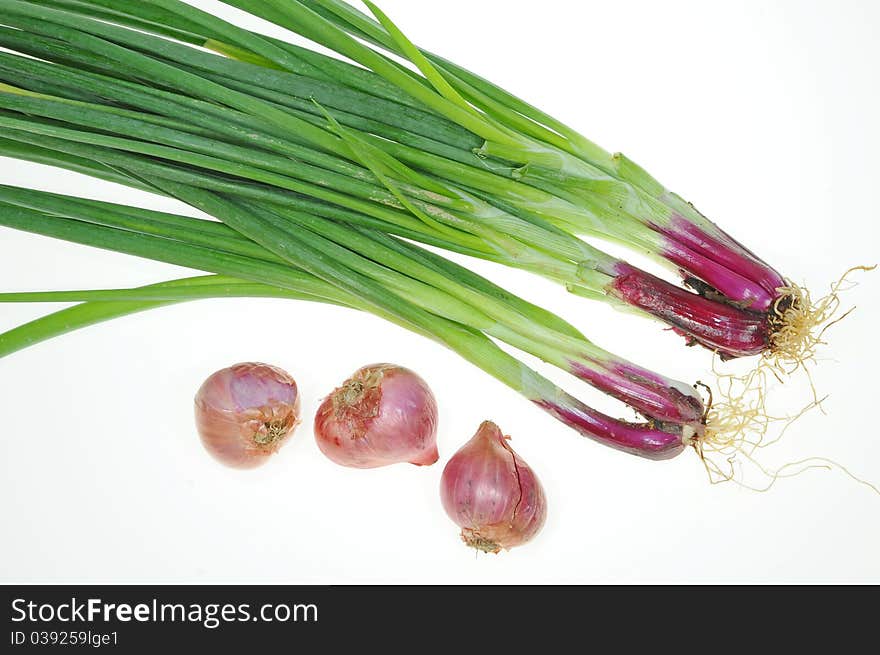 Green Leafy Spring Onions And Red Onions Arranged On A White Background