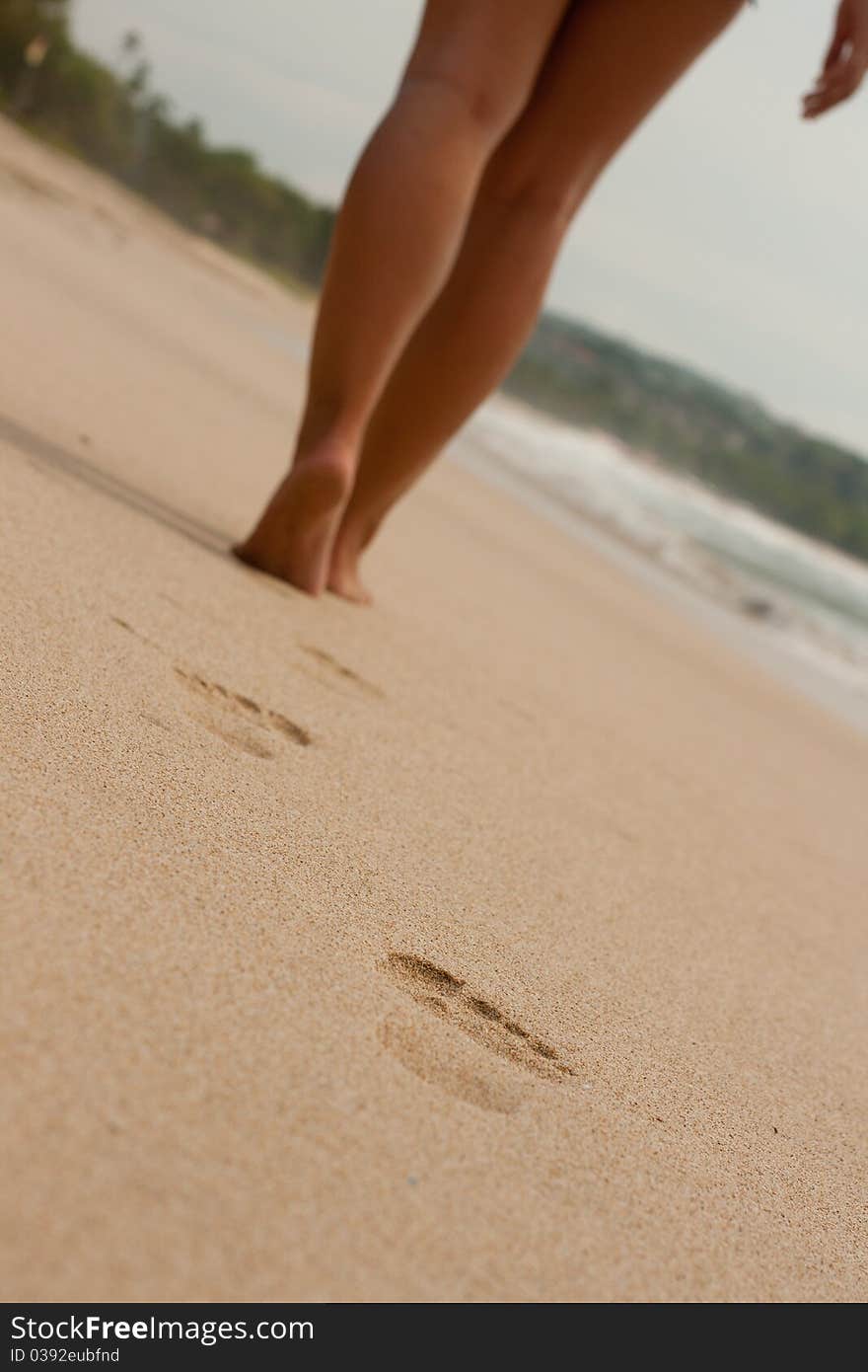 Image of women's legs on the beach and footprints in the sand