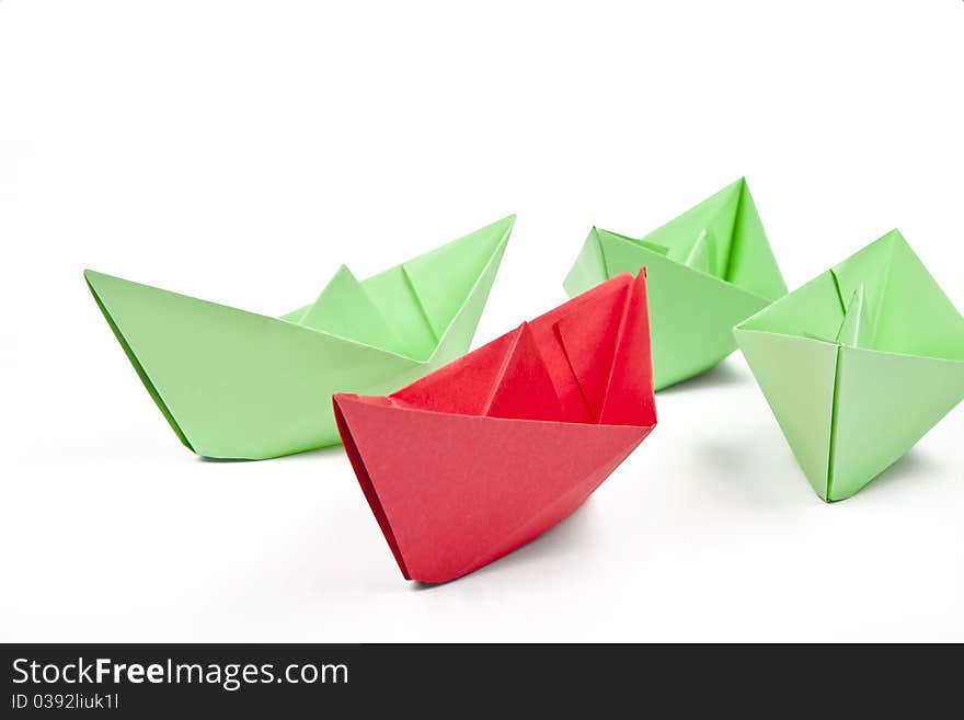 Single red paper boat between lots of green paper boats on white