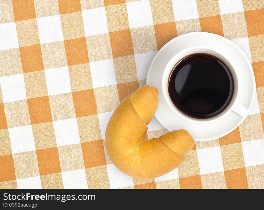 Top view of black coffee cup and croissant on checked tablecloth. Top view of black coffee cup and croissant on checked tablecloth