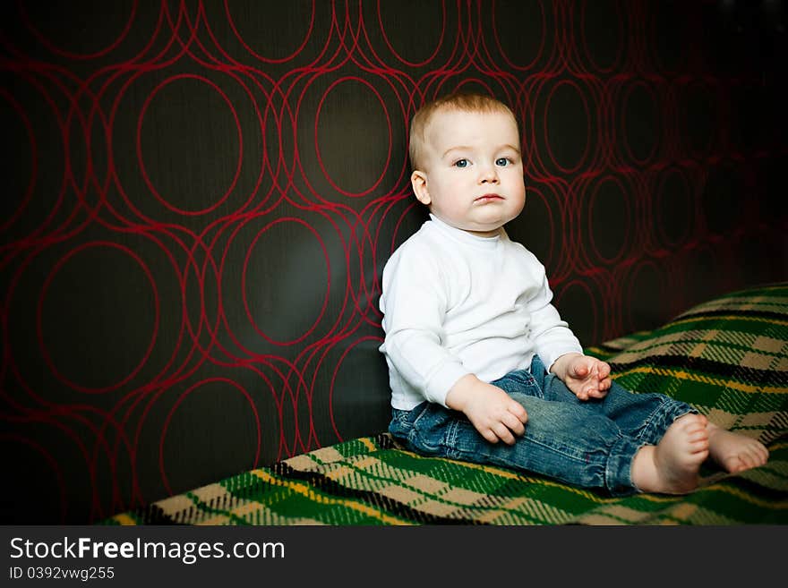 Little serious boy sitting near the wall at home