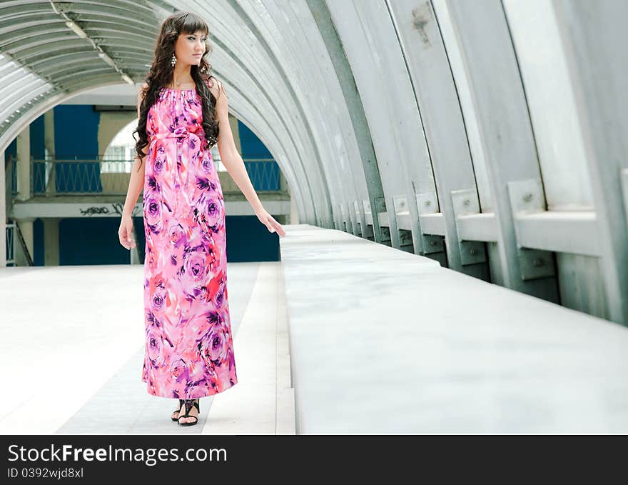 The beautiful girl in a long dress is by the window in a pedestrian crossing