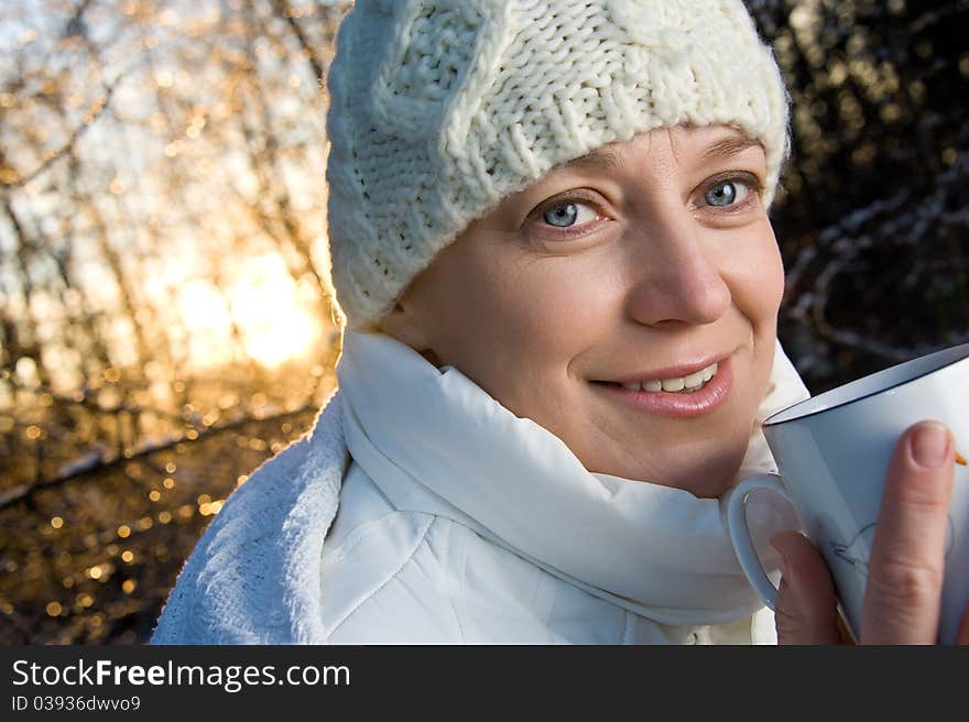 Blue-eyed woman in white, with a mug in his hands, in the winter forest. closeup, portrait