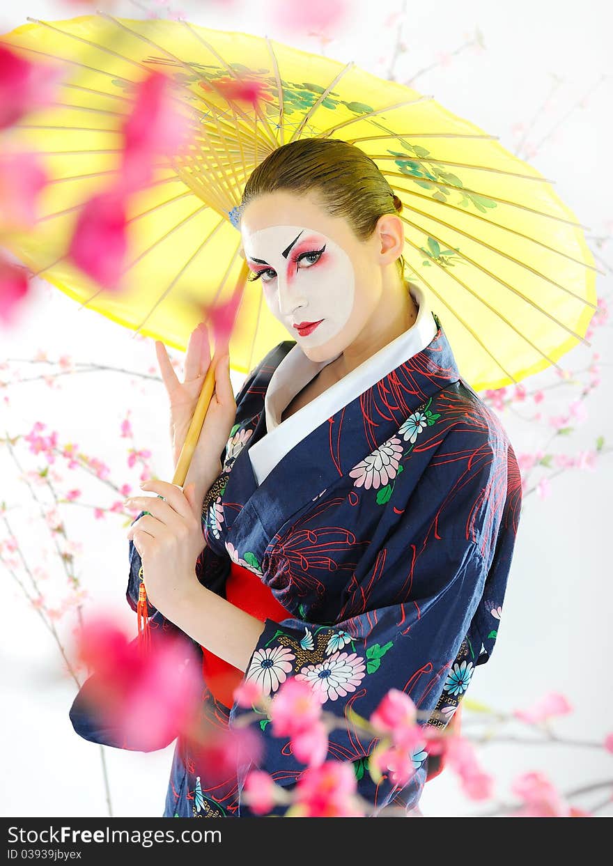 Artistic portrait of japan geisha woman with creative make-up near sakura tree in kimono with umbrella