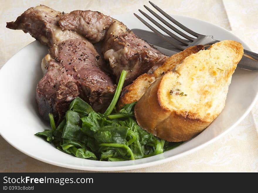 Delicious lamb chops with garlic bread and spinach on a plate