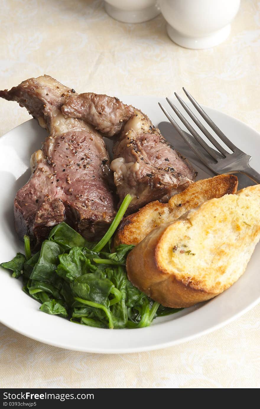 Delicious lamb chops with garlic bread and spinach on a plate