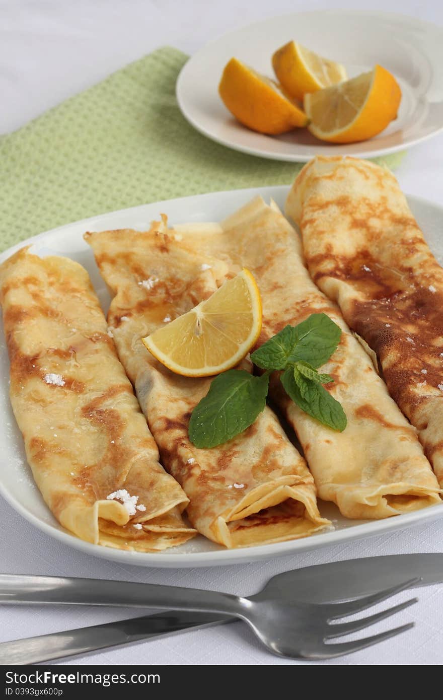 A plate of freshly made sugar and lemon pancakes garnished with fresh mint. Served on a white plate and a green napkin.