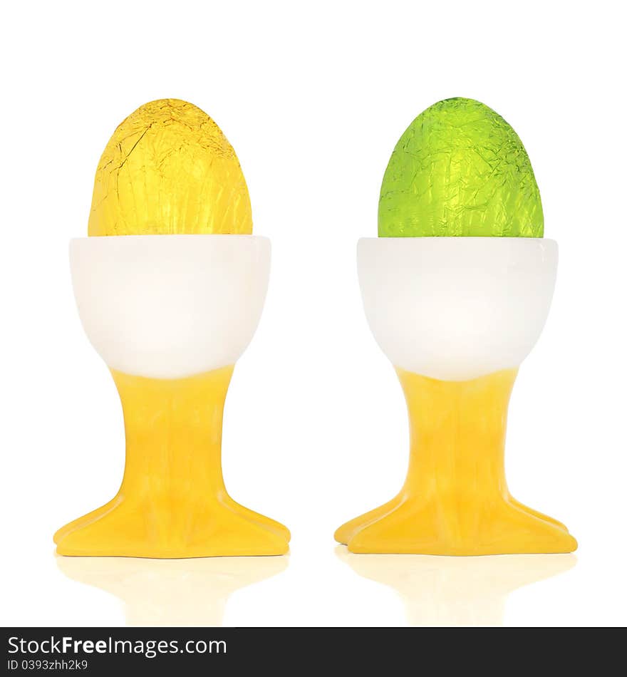 Chocolate easter eggs wrapped in coloured foil, in egg cups, over white background. Chocolate easter eggs wrapped in coloured foil, in egg cups, over white background.