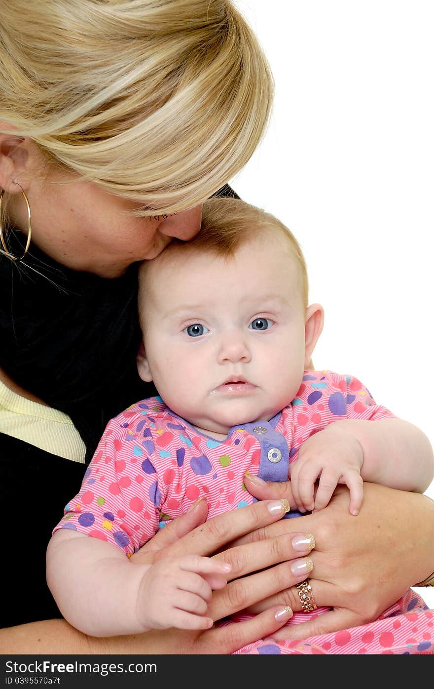 Mother is looking down on her sweet baby while kissing her. Taken on a white background. Mother is looking down on her sweet baby while kissing her. Taken on a white background.