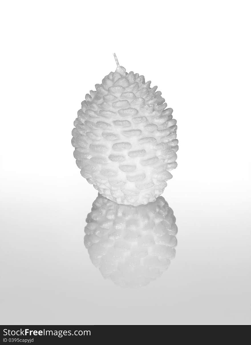 Photograph of a white decorative candle shaped as a pine cone against white background with reflection in foreground. Photograph of a white decorative candle shaped as a pine cone against white background with reflection in foreground