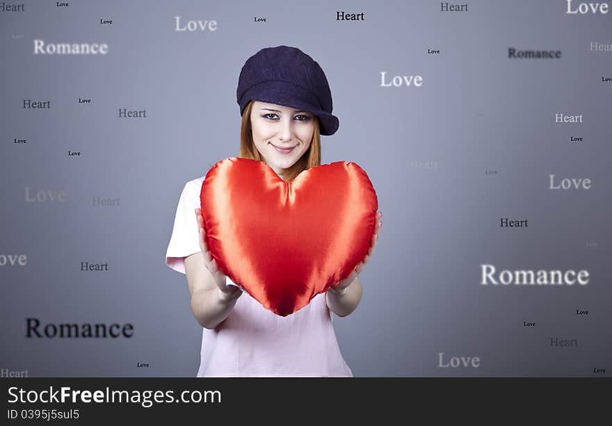 Beautiful red-haired girl in cap with toy heart. Studio shot.