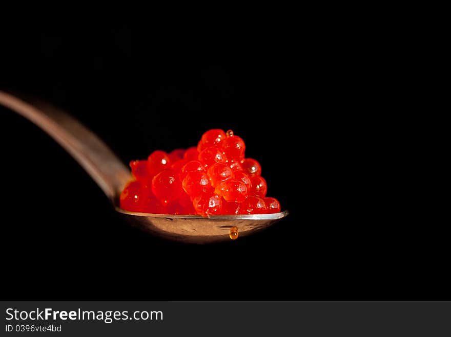 Spoon with red caviar isolated on black background