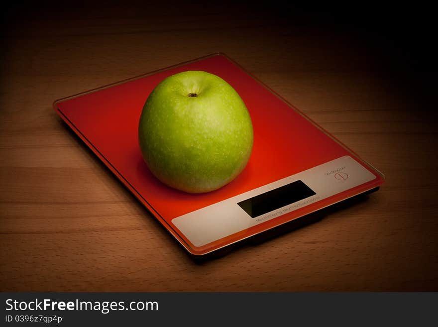 Apple is in the scales, standing on a wooden surface.