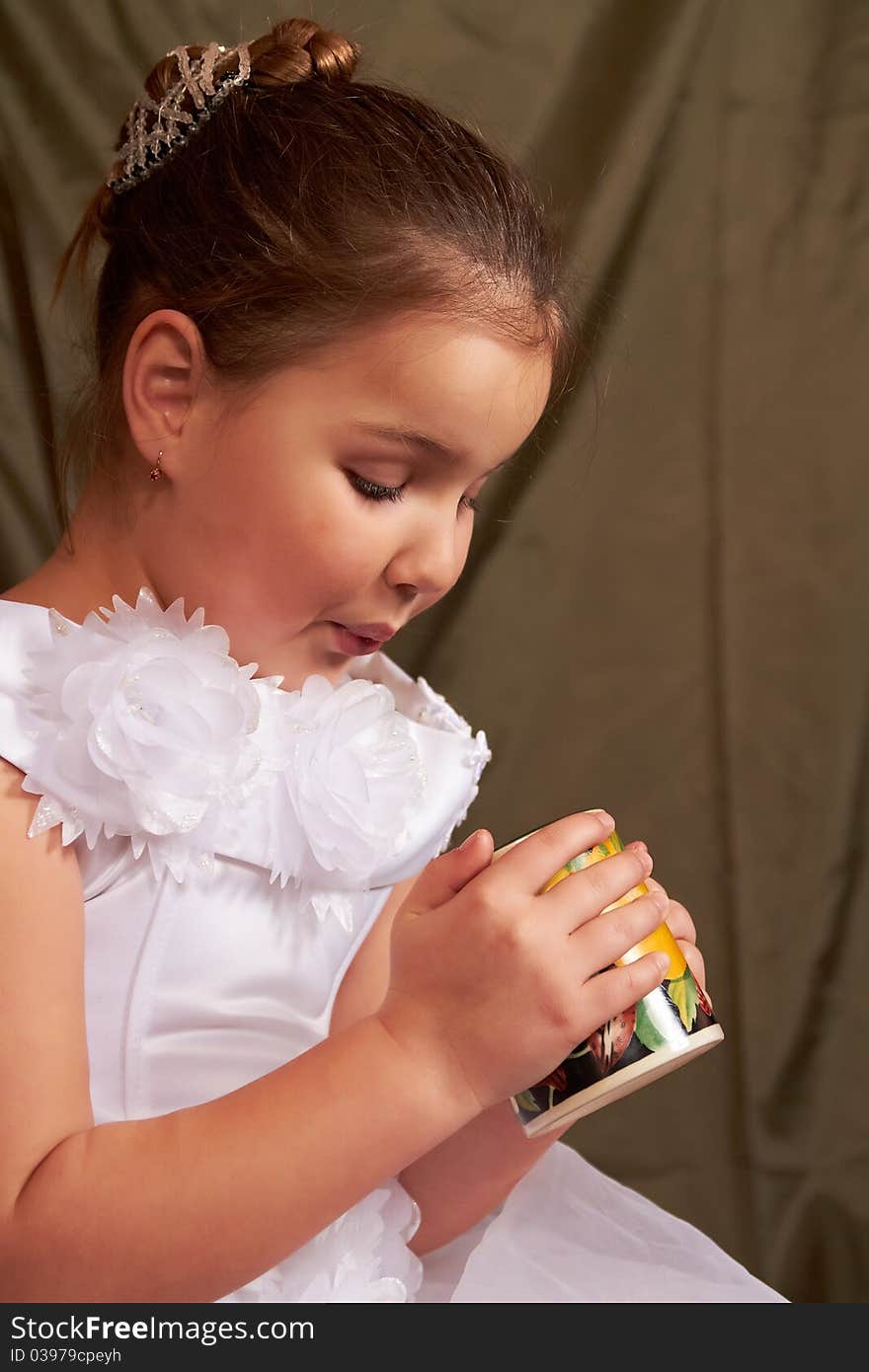 The little girl in a white dress drinks from a large mug. The little girl in a white dress drinks from a large mug.